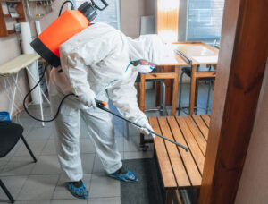 A pest control technician in protective gear spraying an indoor area to eliminate pests